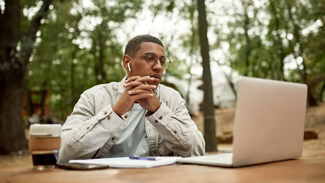 Man sitting outside looking at an open laptop