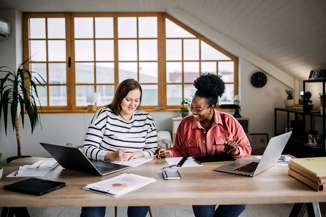 Two women at a table looking down and working together