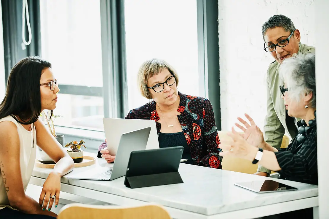 Women sitting around a table with laptops talking